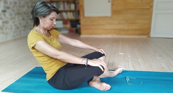 Céline Legg assise sur un tapis, en posture de flexion avant