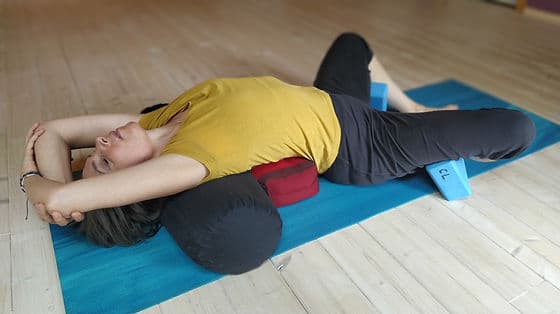 Personne allongée en posture de yoga restauratif, soutenue par un traversin